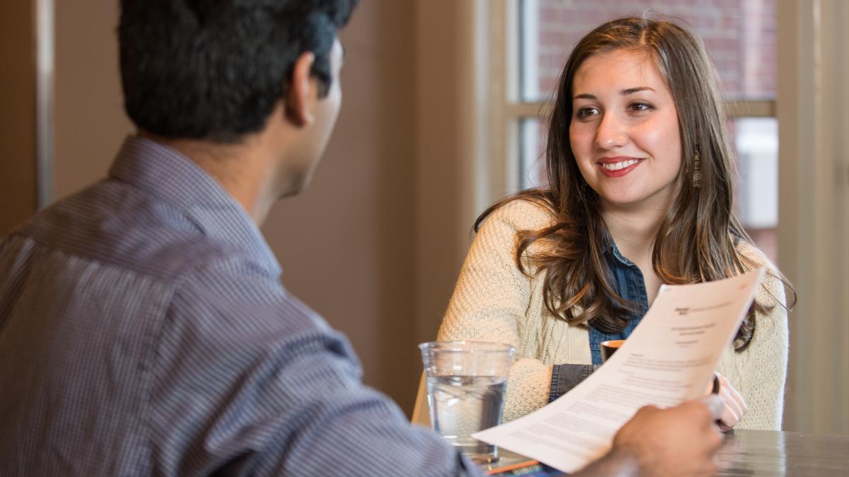 A young A woman smiles while a man with his back to the camera holds a paper.